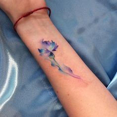 a woman's arm with a small watercolor flower tattoo on the left wrist