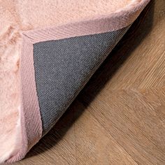 the corner of a pink and black rug on top of a wooden floor with wood grains