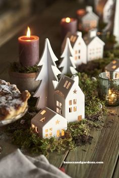 a table topped with small white houses next to candles and plates filled with food on top of it