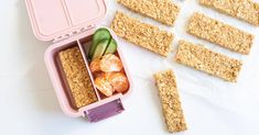 an open lunch box with crackers, fruit and veggies in it on a white surface