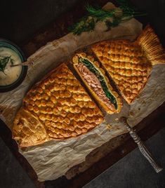 a sandwich cut in half sitting on top of a piece of paper next to a bowl