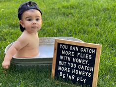 a baby sitting in a metal tub with a sign on the side saying you can catch more flies with honey, but you catch more honeys being fly