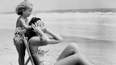 a woman in a bathing suit sitting on a beach chair with her feet up next to the water