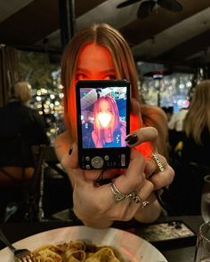 a woman taking a selfie with her cell phone in front of some food and drinks