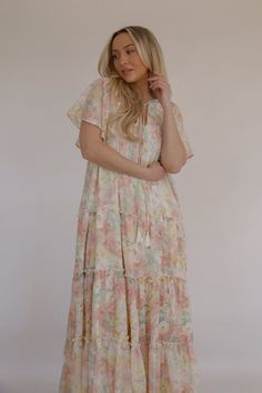 This beautiful Spring Blooms Maxi Dress is perfect for any spring and summer occasion. The flutter sleeves add a feminine touch, while the tiered skirt gives it a flowy, bohemian feel. The stunning floral print adds a pop of color. The maxi length makes it versatile for formal occasions or a casual day out. The lightweight fabric ensures you stay cool and comfortable in warm weather. colors in the dress: pink, white, green and yellow lined relaxed loose fit flutter sleeves smocked top tiered ski Flowy Multicolor Tiered Dress For Spring, Multicolor Flowy Tiered Dress For Spring, Feminine Flowy Floral Print Tiered Dress, Flowy Feminine Tiered Dress With Floral Print, Feminine Flowy Tiered Dress With Floral Print, Flowy Floral Dress With Ruffle Hem And Tiered Skirt, Flowy Pink Tiered Dress For Vacation, Spring Multicolor Tiered Dress, Summer Tiered Boho Print Dress