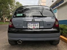 the back end of a gray car parked in front of a building with a sign on it