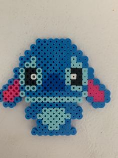 a blue bead art piece with black eyes and pink nose sitting on a white surface