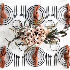 an arrangement of flowers and napkins on a white table cloth with black circles in the background