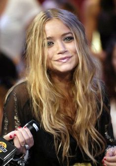 a woman with long blonde hair holding a microphone in her hand and looking at the camera