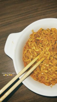 two chopsticks sticking out of a bowl of noodles with sauce on the side