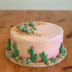 a pink cake with green frosting and cactus decorations on the top is sitting on a wooden table