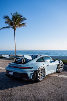 a blue sports car parked on the side of the road near the ocean and palm trees