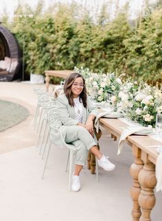 a woman sitting at a table with white flowers and greenery on the tables in front of her