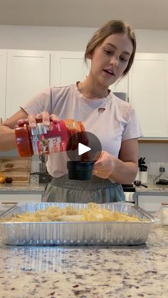 a woman pouring something into a container on top of a counter in front of some food