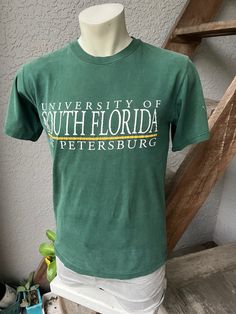 This amazing genuine 1990s vintage tee is from the University of South Florida Bayboro campus in St. Petersburg. Not sure what shade of green this shirt started as, but it has since faded to a nice deep olive color with a hint of blue. It is perfectly distressed and in excellent vintage condition. The ONLY flaw is faint dot on the the sleeve as shown. Still awesome! Made in the USA by Cotton Exchange - 100% cotton. Check the measurements: SIZE: Pit to pit: 19.5" Sleeves: 8.5" Collar to hem: 25.5 University Of South Florida, Olive Color, South Florida, St Petersburg, Vintage Tees, Vintage Tshirts, Shades Of Green, Favorite Outfit, University