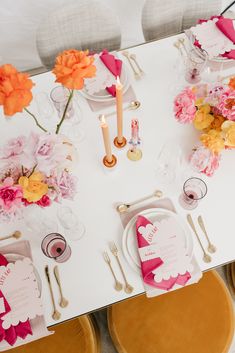 the table is set with pink and yellow flowers, candles, and place settings for dinner