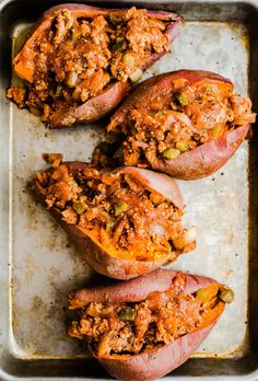 three stuffed sweet potatoes on a baking sheet with meat toppings and seasoning sprinkled on top