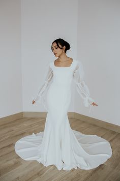 a woman in a white wedding dress standing on a wooden floor with her arms outstretched