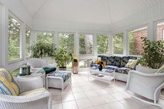 a sun room with white wicker furniture and large windows on the side of it