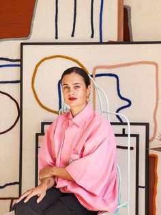 a woman sitting on top of a chair in front of a wall with abstract paintings