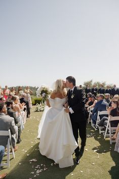 a bride and groom kiss as they walk down the aisle at their outdoor wedding ceremony