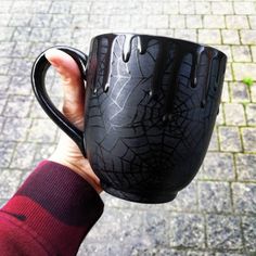 a hand holding a black coffee cup with spider webs on it