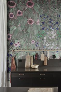 a wall with flowers painted on it next to a table and cabinets in front of a window