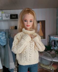 a doll with blonde hair wearing a white sweater and blue jeans in a room full of clothes