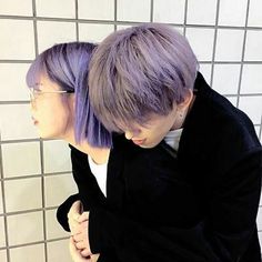 two people standing next to each other in front of a wall with white tiles on it