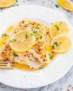 a white plate topped with fish covered in lemon slices