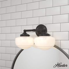 a bathroom mirror with two lights on it next to a white tiled wall and floor