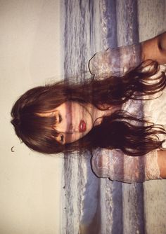 a woman with long hair standing next to a curtain