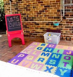 an outdoor play area with letters and numbers on the floor, in front of a brick wall