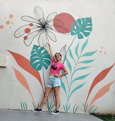 a woman standing in front of a wall with flowers painted on it and holding her arm up