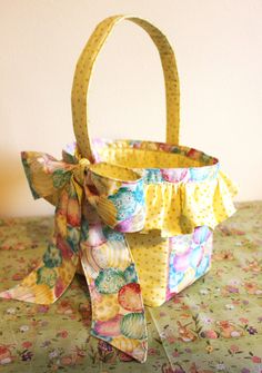 a small yellow basket with a bow on top of a floral table cloth covered table