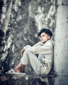 a young man sitting on top of a cement wall next to a tree filled forest