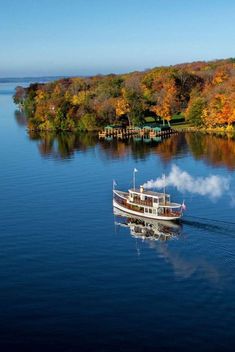 a boat traveling on the water in front of trees with autumn foliages around it