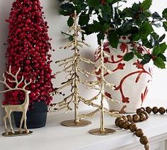 three christmas trees on a mantel with beads and ornaments in front of the fireplace