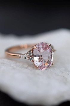 a close up of a ring with an oval shaped pink stone and diamond accents on it