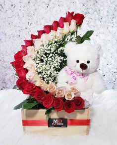 a white teddy bear sitting in a box with roses