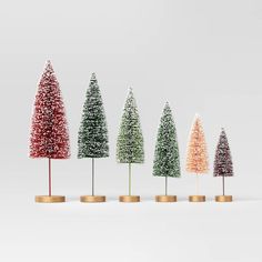 five small christmas trees are lined up in different colors and sizes, with gold bases