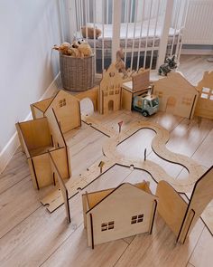 a wooden model of a house with cars and buildings on the floor next to it