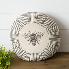 a black and white bee pillow sitting on top of a wooden table next to a potted plant