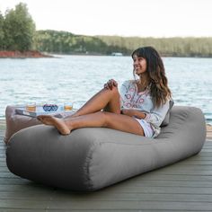 a woman sitting on an inflatable bean bag chair by the water with a tray of food