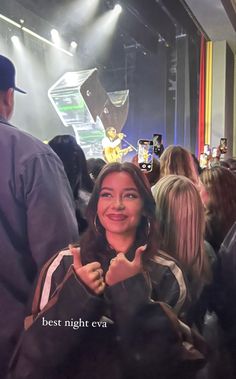 a woman giving the thumbs up sign in front of a group of people at a concert