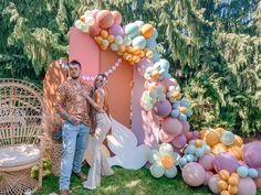 two people standing next to each other in front of a balloon arch with balloons on it