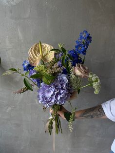 a person holding a bouquet of flowers in their hand and wearing a white shirt with tattoos on his arm