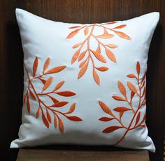 a white pillow with orange leaves on it sitting on top of a wooden chair next to a wall