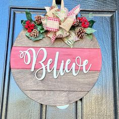 a wooden sign that says believe hanging on a door with pine cones and red berries