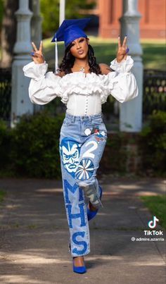 a woman dressed in jeans and a graduation cap is walking down the street with her hands up